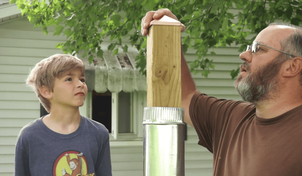 A father and son placing a cap on the pole.