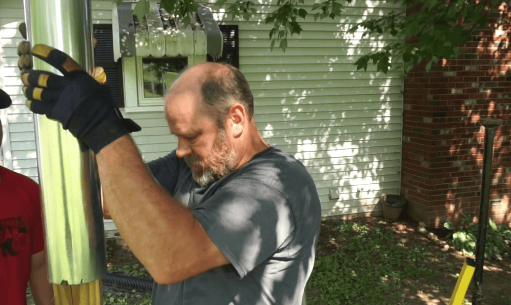 A man installing a hook on the pole for the bird feeder.