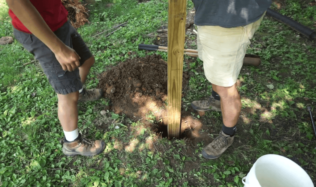 A father and son placing a pole in the hole to hang a bird feeder.