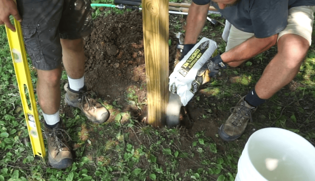 A man pouring concrete into a hole with a pole.