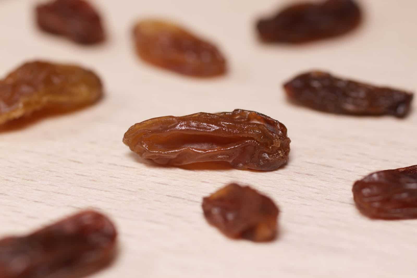 10 Grocery Store Foods That Attract the Most Colorful Birds 8 Detailed close-up image of dried raisins artfully arranged on a light wooden surface.